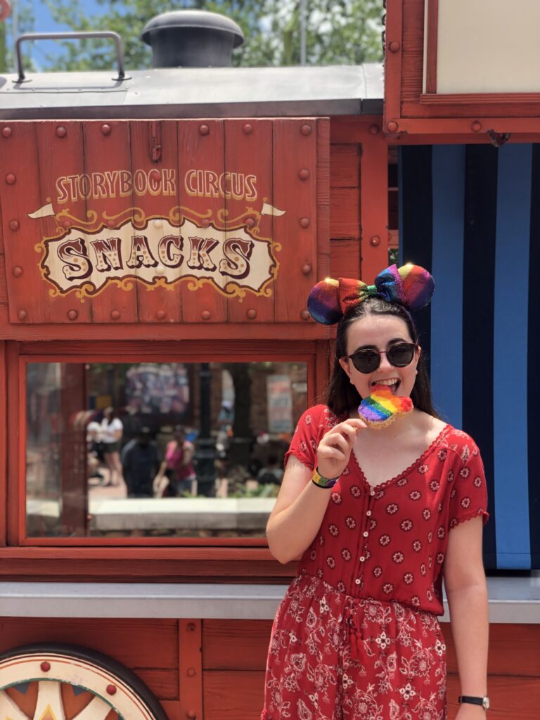 A girl eating a Mickey Mouse shaped Rice Krispy treat in front of a cart that says 'Snacks'