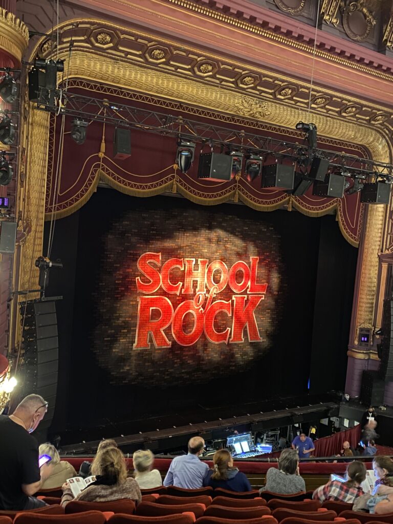 The image is a view of the School Of Rock Stage, with the School Of Rock logo on display.