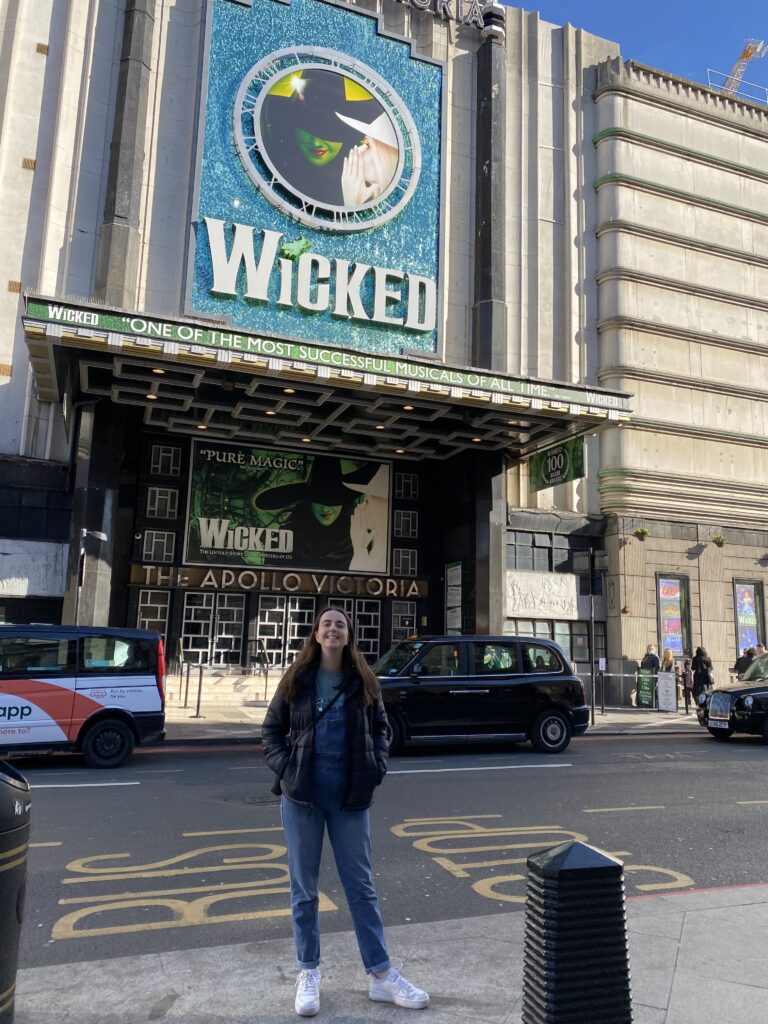 A girl standing outside of the Apollo Victoria theatre in London where Wicked currently plays.